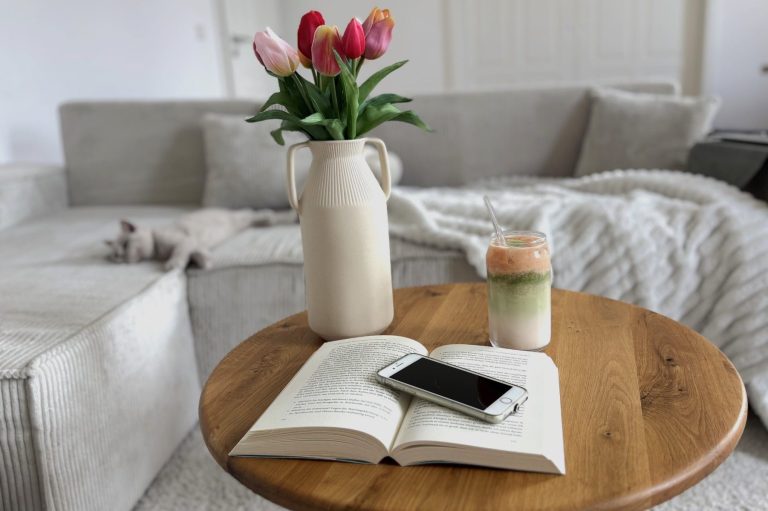 Ein Tisch mit einem Buch, einem Handy, einem Getränk und einer Vase mit Tulpen.
